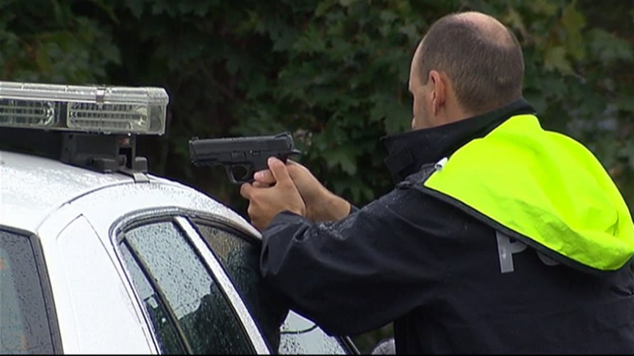 Un policier pointe son arme ver la demeure où le suspect demeurait terré.