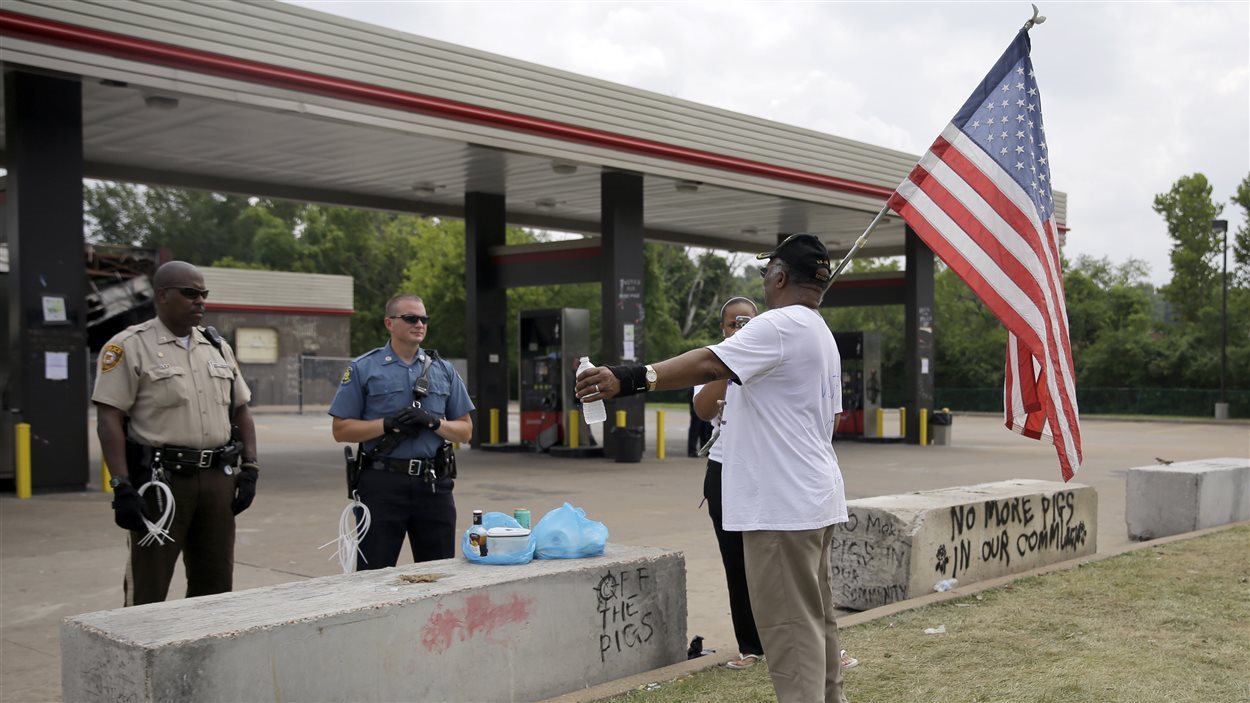 Un homme portant un drapeau américain discute avec des policiers près d'une station-service de Ferguson.