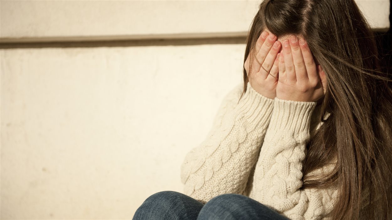Une fille cache son visage dans ses mains.