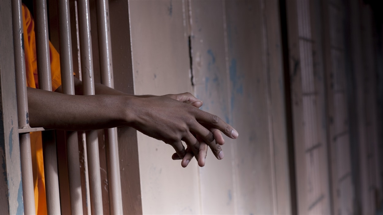 Les mains d'un prisonnier sortent des barreaux d'une cellule.