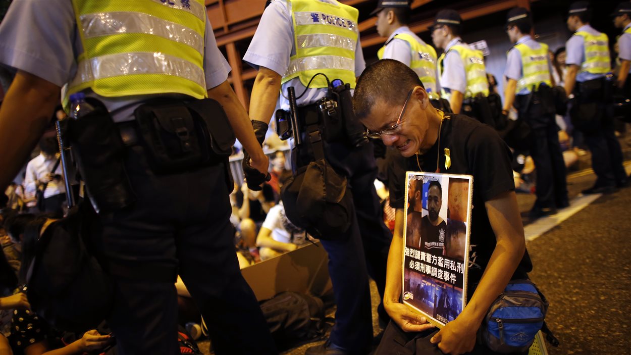 Un manifestant en pleurs porte une pancarte réclamant une enquête sur la mise à tabac présumée d'un autre protestataire, Ken Tsang Kin-chiu, par les policiers au cours de la nuit.