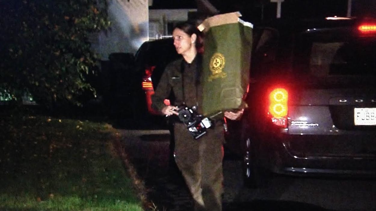 Une policière quitte la maison du suspect abattu avec un sac de documents.