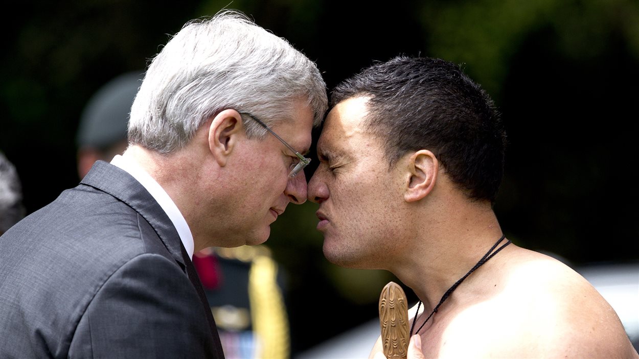 Stephen Harper exécute la salutation de bienvenue en pressant son nez sur celui d'un guerrier Maori.