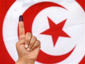 Une Tunisienne montre son doigt taché d'encre devant un drapeau du pays, après avoir voté dimanche. 
