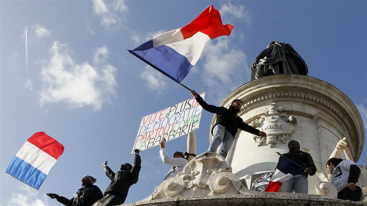Des manifestants sont montés sur une statue au centre de la Place de la République, à Paris, pour brandir des drapeaux français.