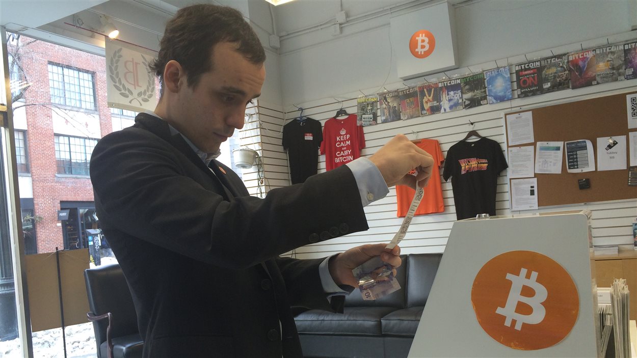 Francis Pouliot, directeur des affaires publiques de l'Ambassade Bitcoin à Montréal, insère un billet dans le guichet automatique afin d'acheter des bitcoins.