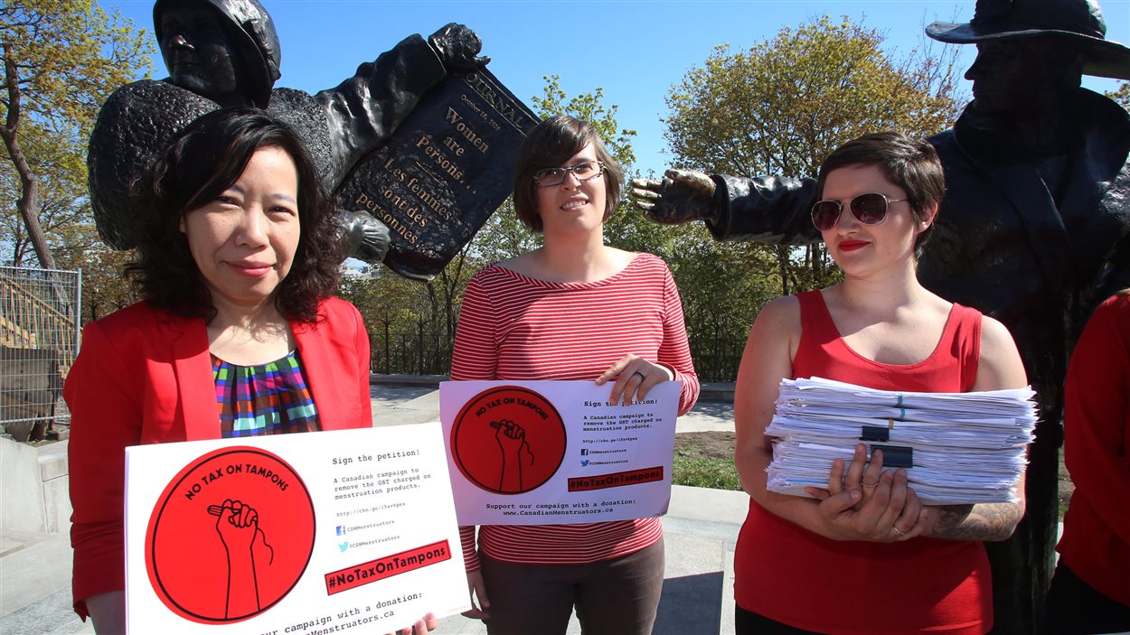 Trois femmes soutenant la campagne de Canadian Menstruators devant la statue de Célèbres cinq, sur la colline Parlementaire.
