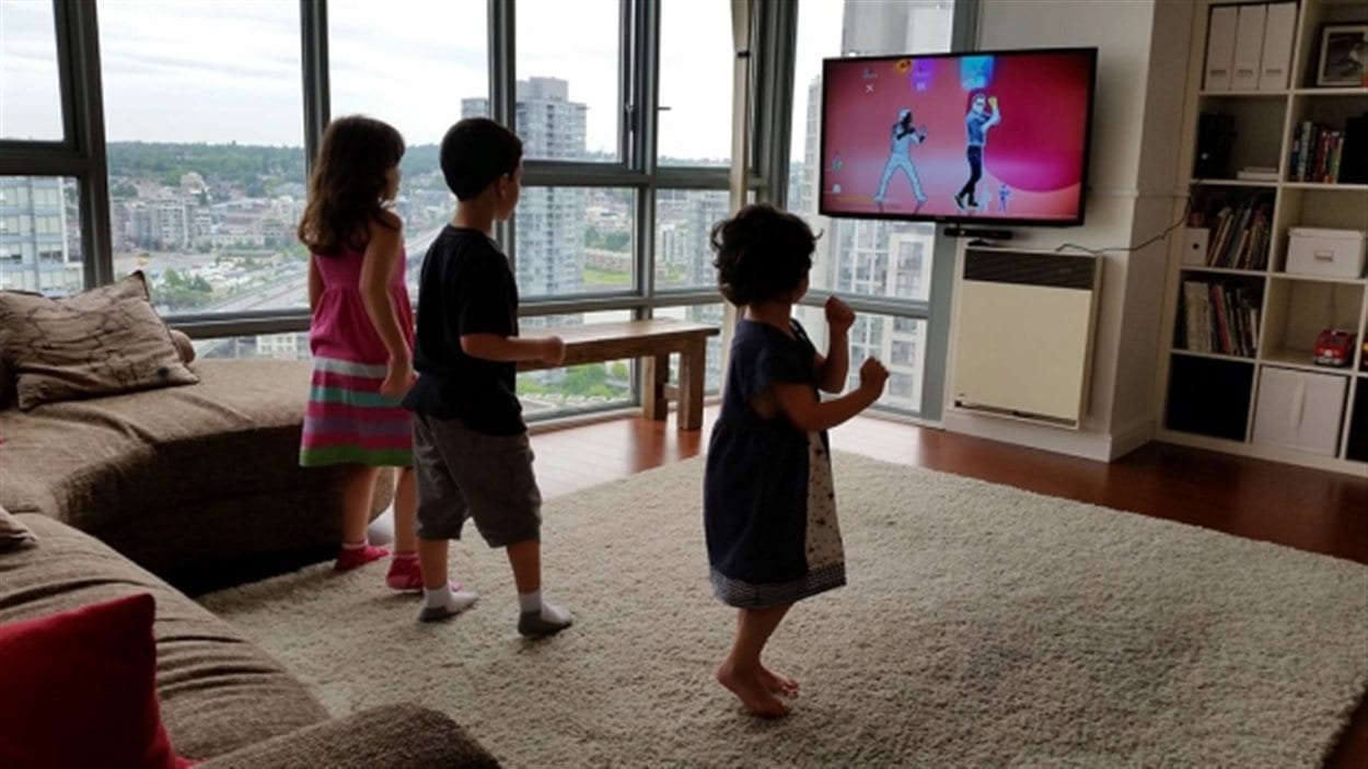 DEs enfants dansent devant une télévision dasn un appartement avec vue sur Vancouver