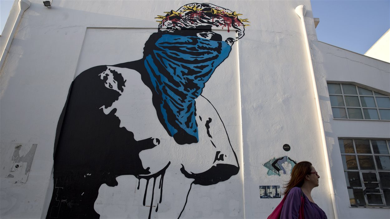 Une Grecque marche devant l'oeuvre d'une artiste de rue française intitulée « Athènes contre l'Europe, résister contre se soumettre ».