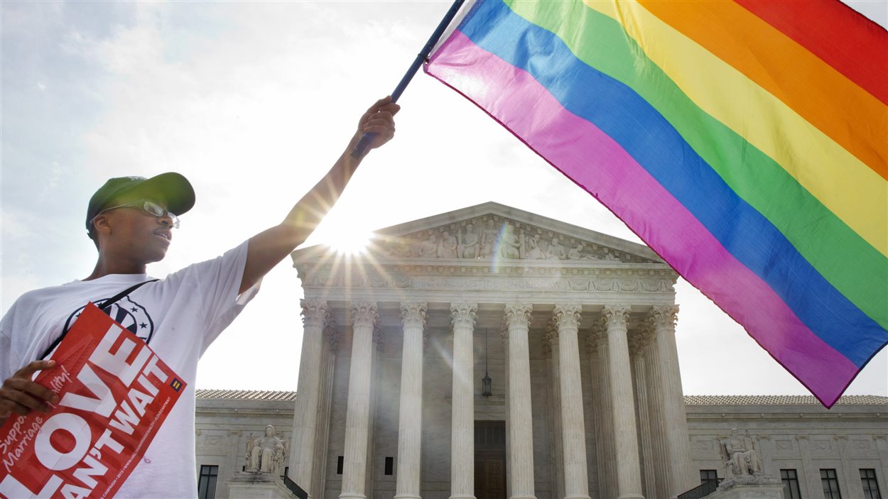 Un homme brandit le drapeau arc-en-ciel de la fierté gaie devant l'édifice de la Cour surprême, à Washington, le 26 juin.