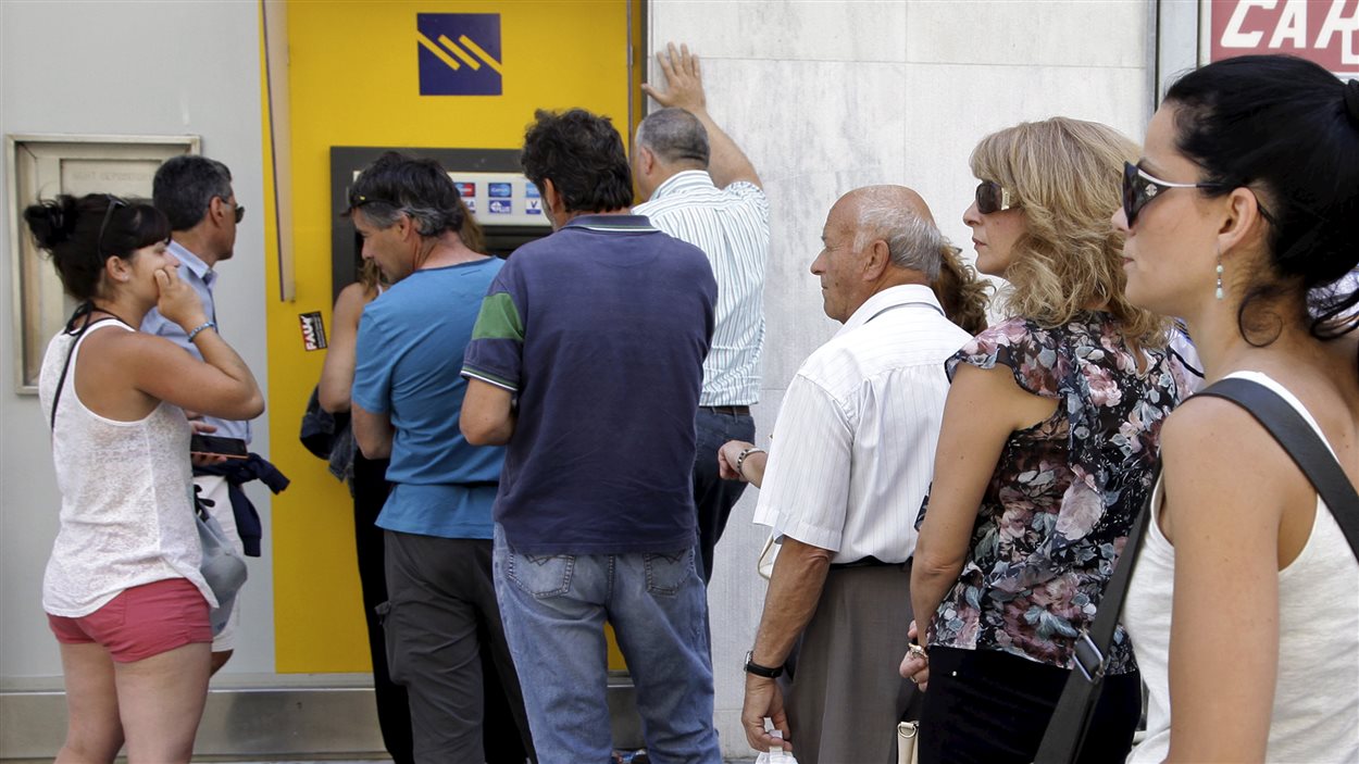 Des personnes font la file pour retirer de l'argent d'un guichet automatique devant une banque de l'île de Crète.