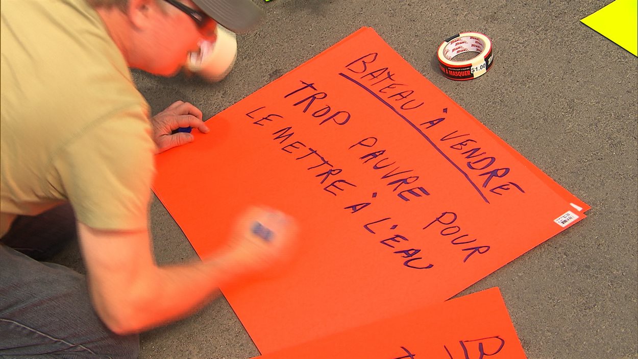 Un homme prépare une pancarte pour montrer son mécontentement face aux hausses des tarifs pour les rampes de mises à l'eau des municipalités.
