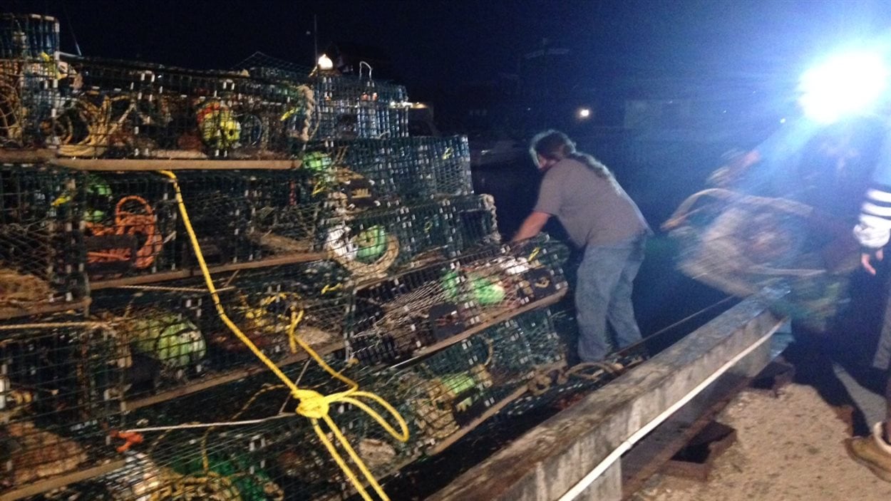 Des pêcheurs chargent des cages à homard sur un bateau.