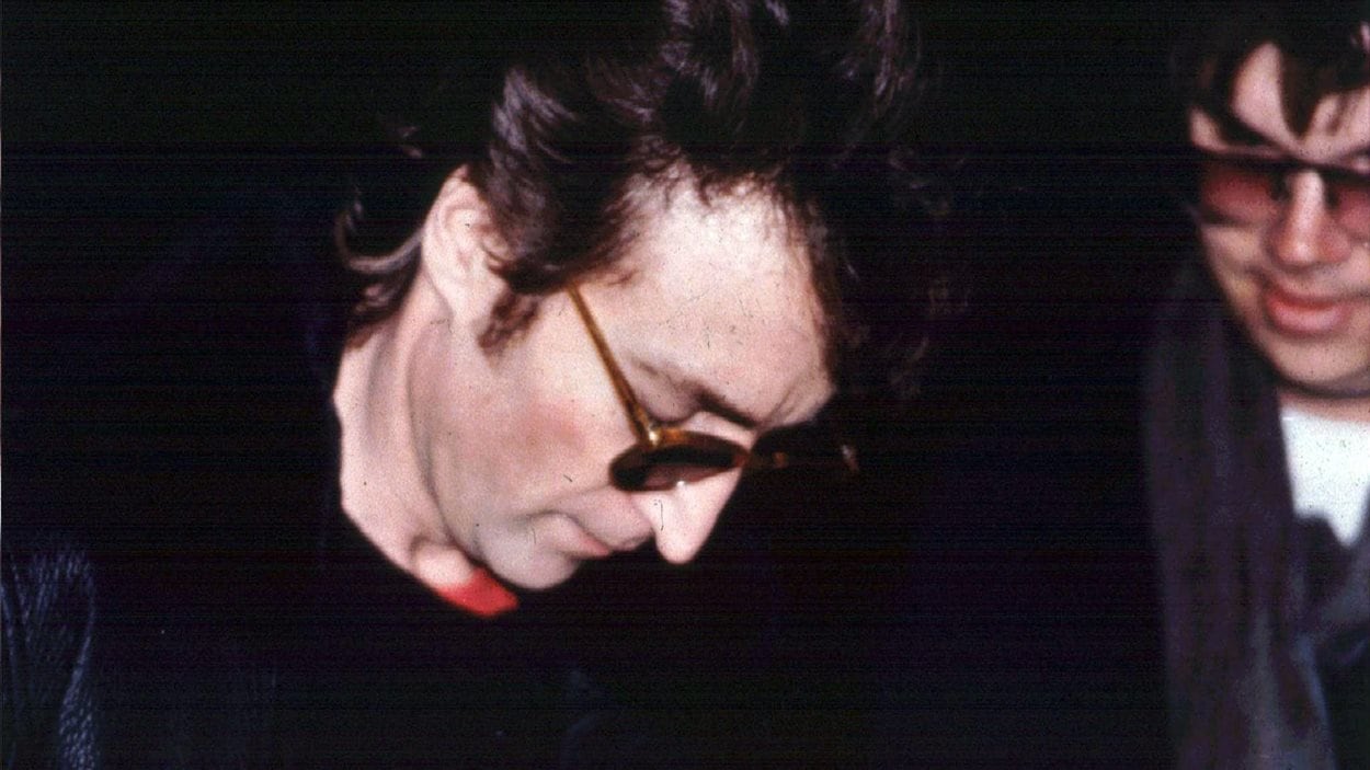 John Lennon autographie un album pour Mark David Chapman (à droite), à la sortie de son appartement de New York le 8 décembre 1980.