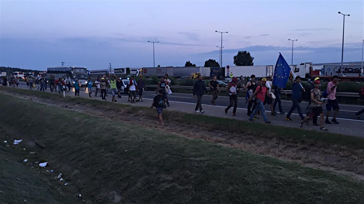 Des migrants, bloqués à la gare de Budapest, ont décidé de marcher vers l'Autriche. À la tête de la file, un migrant tient un drapeau européen.