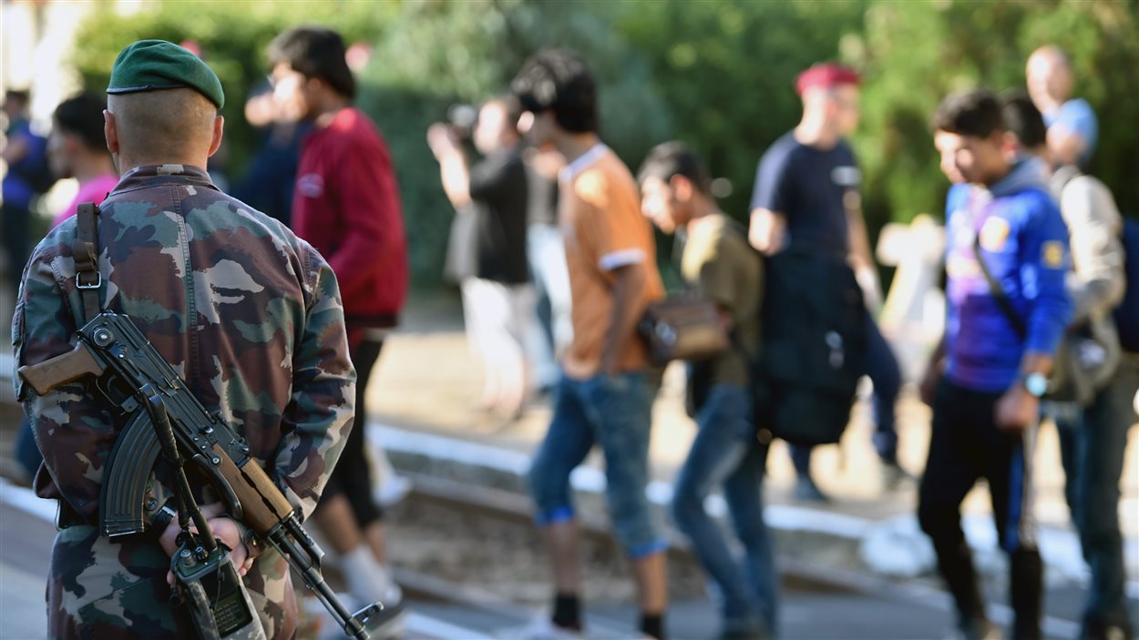 Des migrants montent dans un train sous l'oeil vigilant d'un soldat hongrois à Magyarboly.