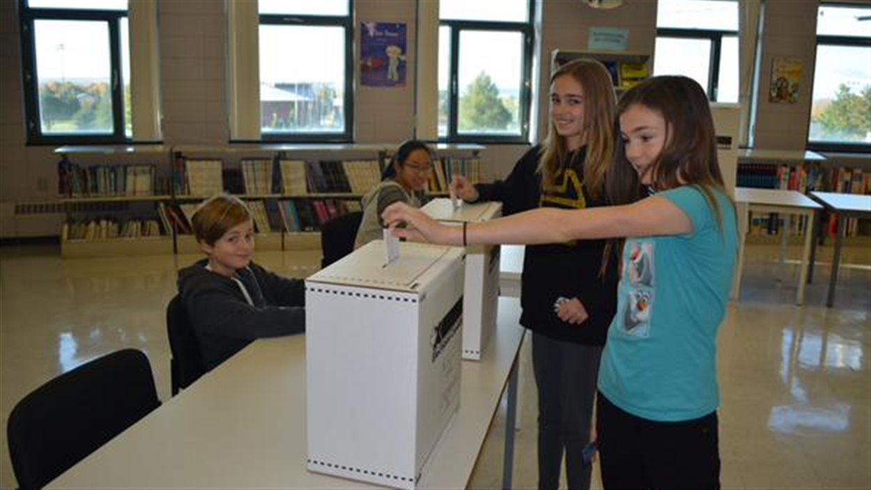 Des élèves de l’école secondaire des pionniers à Saint-Augustin-des-Desmaures, au Québec, déposent leur bulletin de vote.