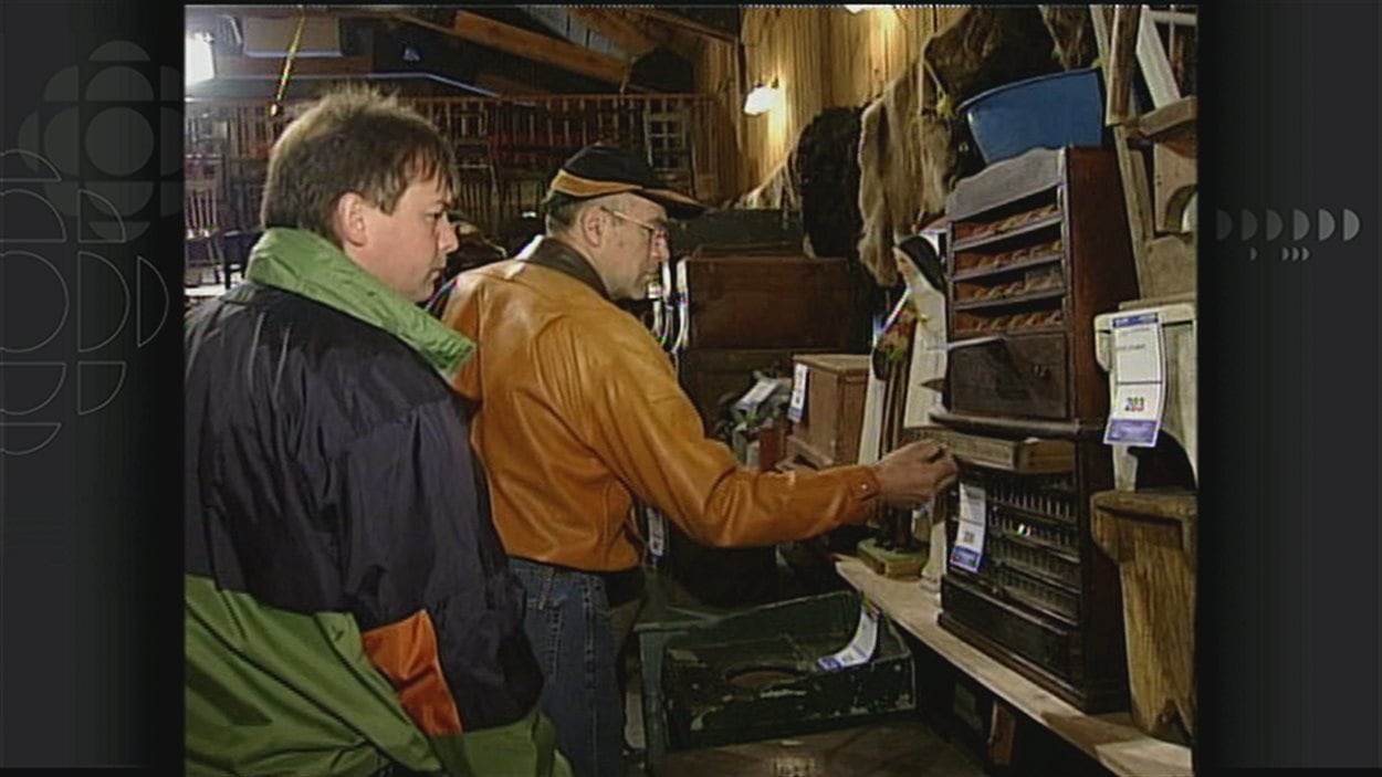 Des acheteurs potentiels inspectent les objets mis en vente à l'encan au Village d'Émilie (2002)