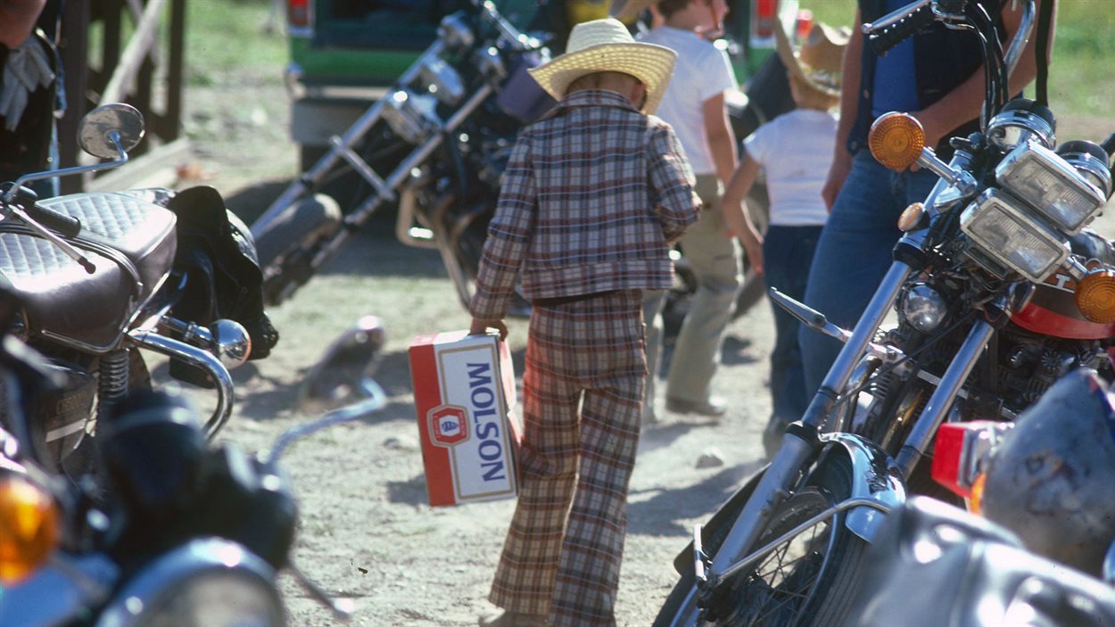 Photographie de François Ruph montrant un enfant qui transporte une caisse de bière dans une fête de motocyclistes à Notre-Dame-du-Nord.
