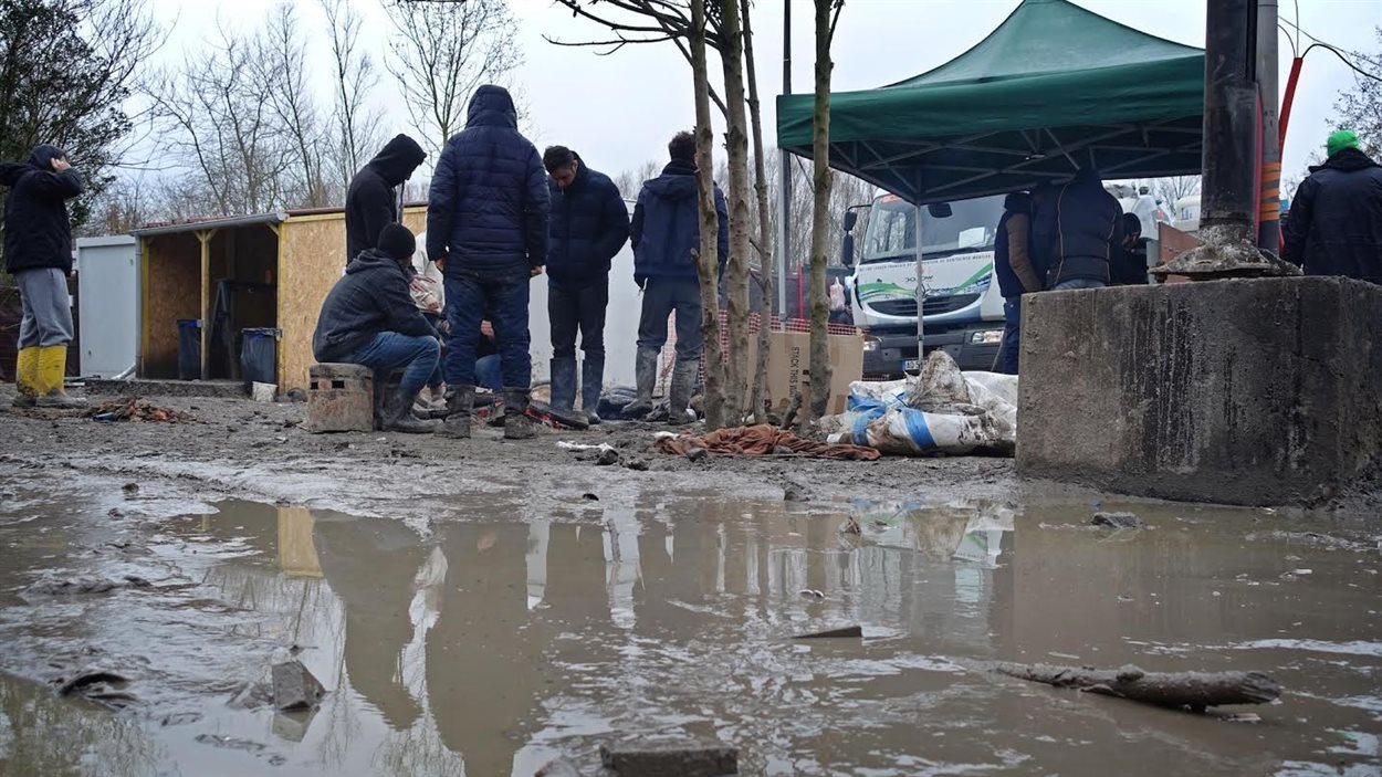 Des réfugiés du camp de Grande-Synthe parlent devant une immense flaque de boue.
