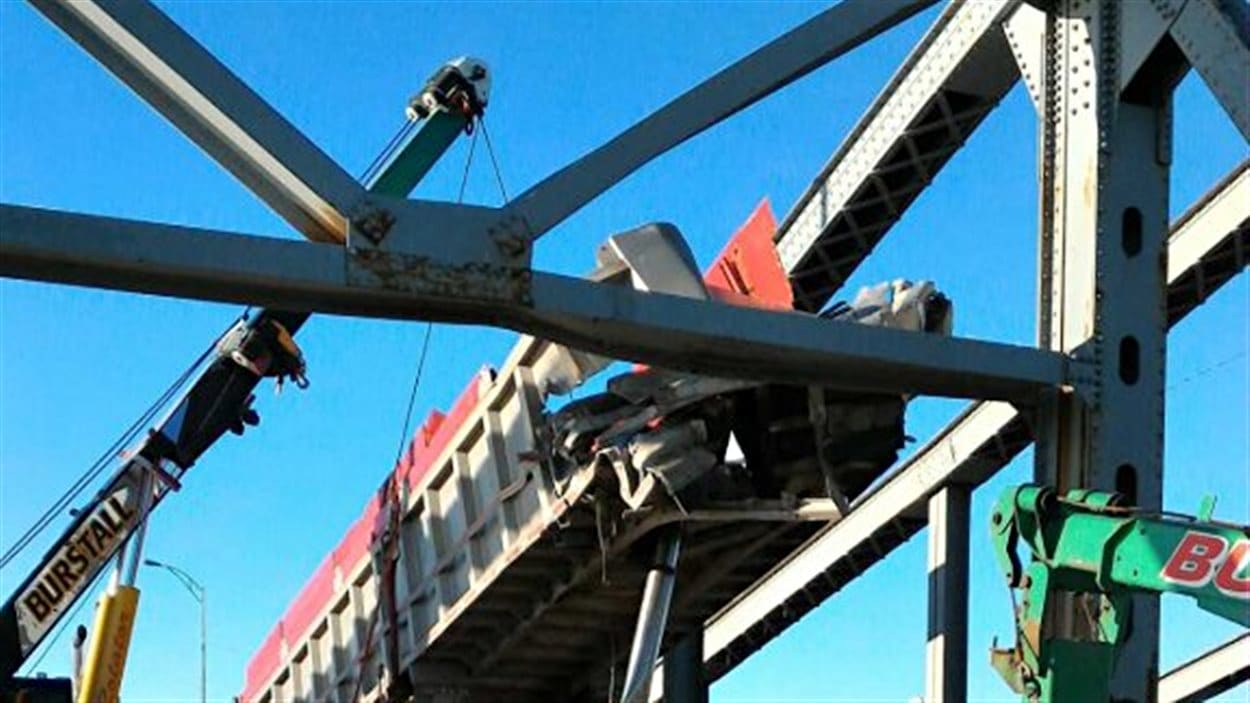 Une équipe s'affaire à retirer une benne d'un camion coincée dans la structure du pont Mercier.
