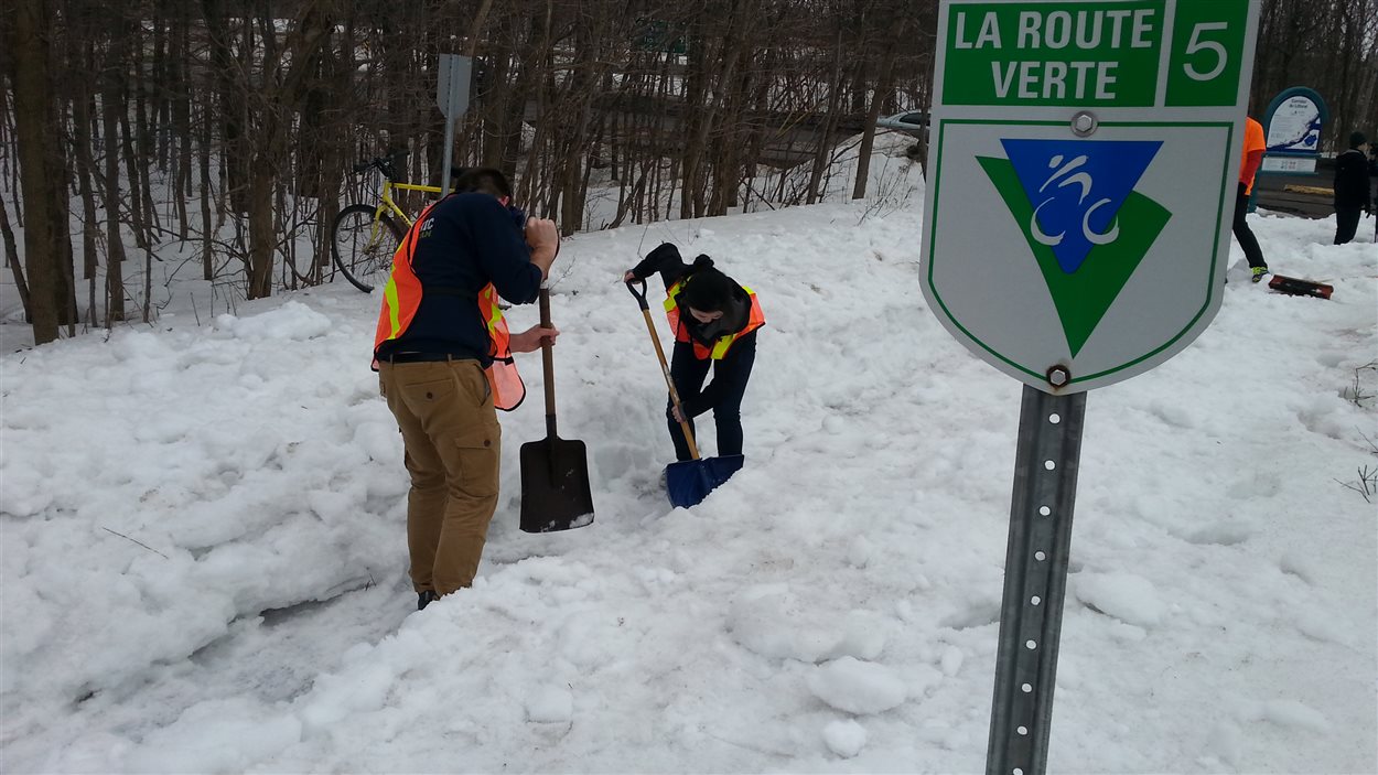 Des citoyens déneigent une piste cyclable près de l'entrée nord du pont de Québec.