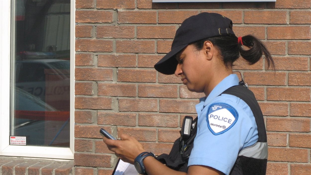 Une policière du SPVM regarde son téléphone cellulaire