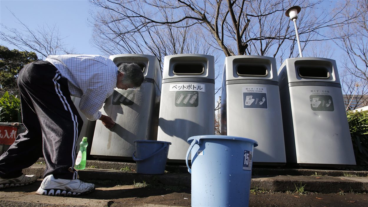Un homme nettoie des bacs à ordures et à recyclage dans un parc de Tokyo, au Japon.