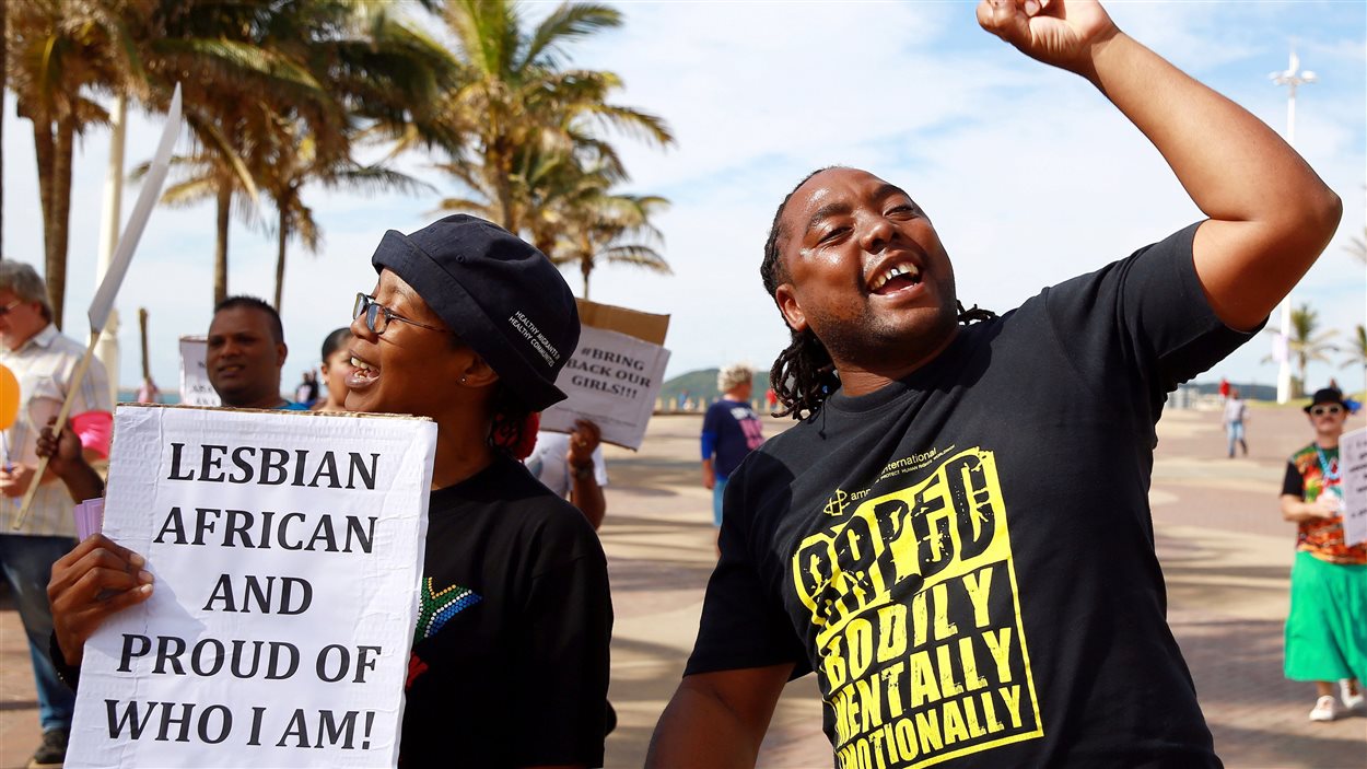 Deux militants pour les droits des homosexuels manifestent, dont une qui tient une pancarte qui dit : « Africaine lesbienne et fière de qui je suis! »