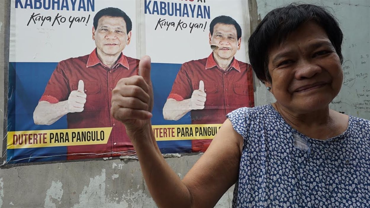 Estella Boromeo sourit et lève le pouce en posant devant une affiche de Rodrigo Duterte en juin 2016 aux Philippines.