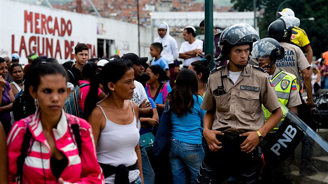 La police surveille les citoyens qui font la file pour acheter l'épicerie à Caracas, au Venezuela, le 11 juin 2016.