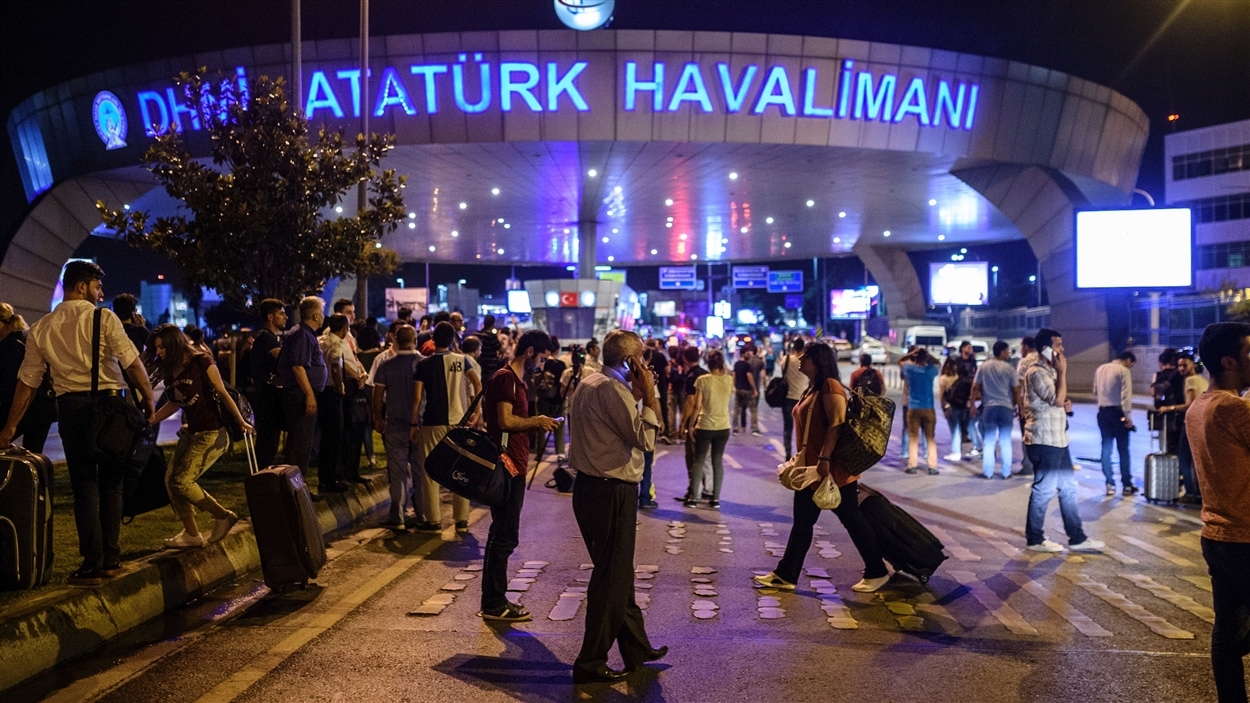 Plusieurs voyageurs attendent près de l'entrée de l'aéroport d'Istanbul après que des attentats-suicides y soient survenus.