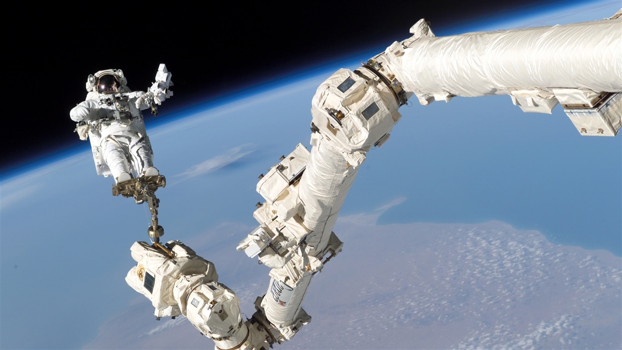 Un astronaute arrimé au Canadarm, le « bras spatial canadien » attaché à une navette spatiale américaine