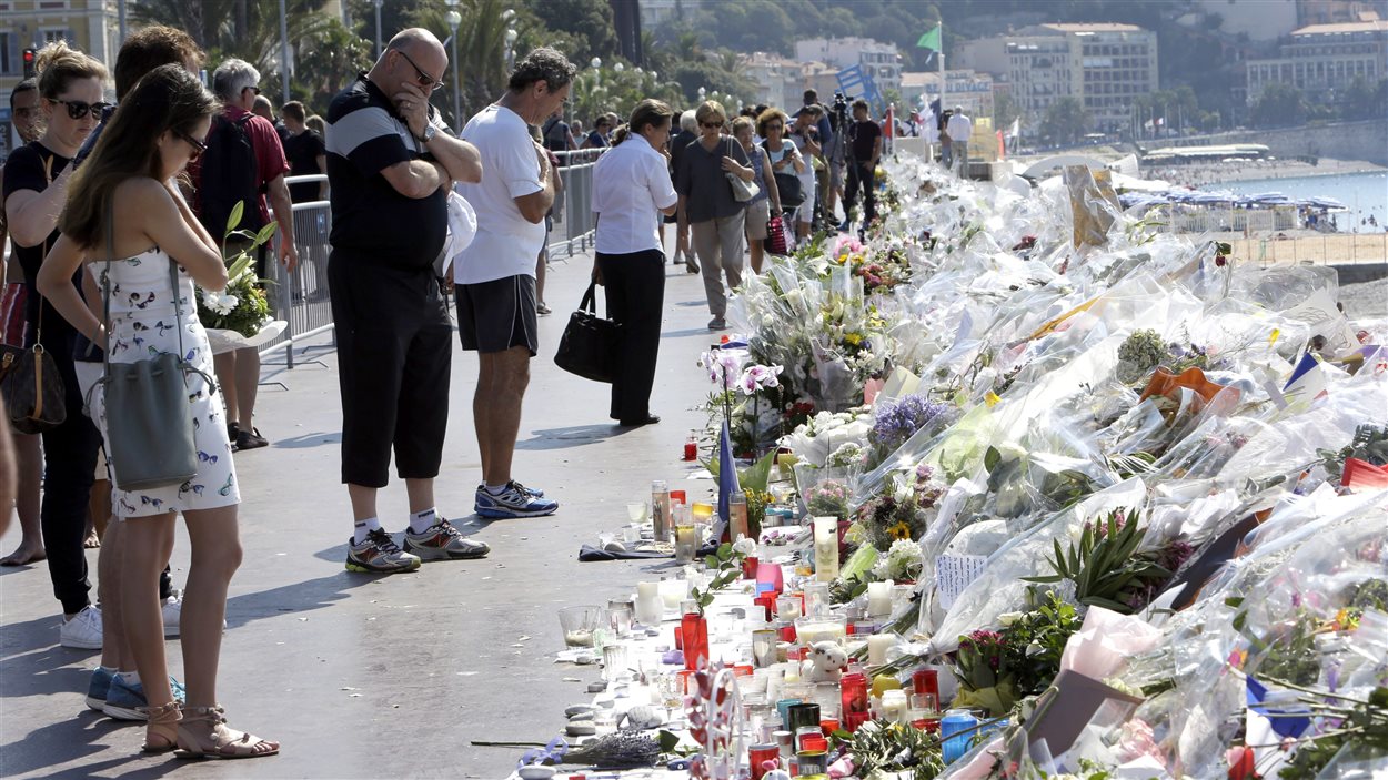 Des gens devant des fleurs déposées le long de la promenade des anglais, à Nice.