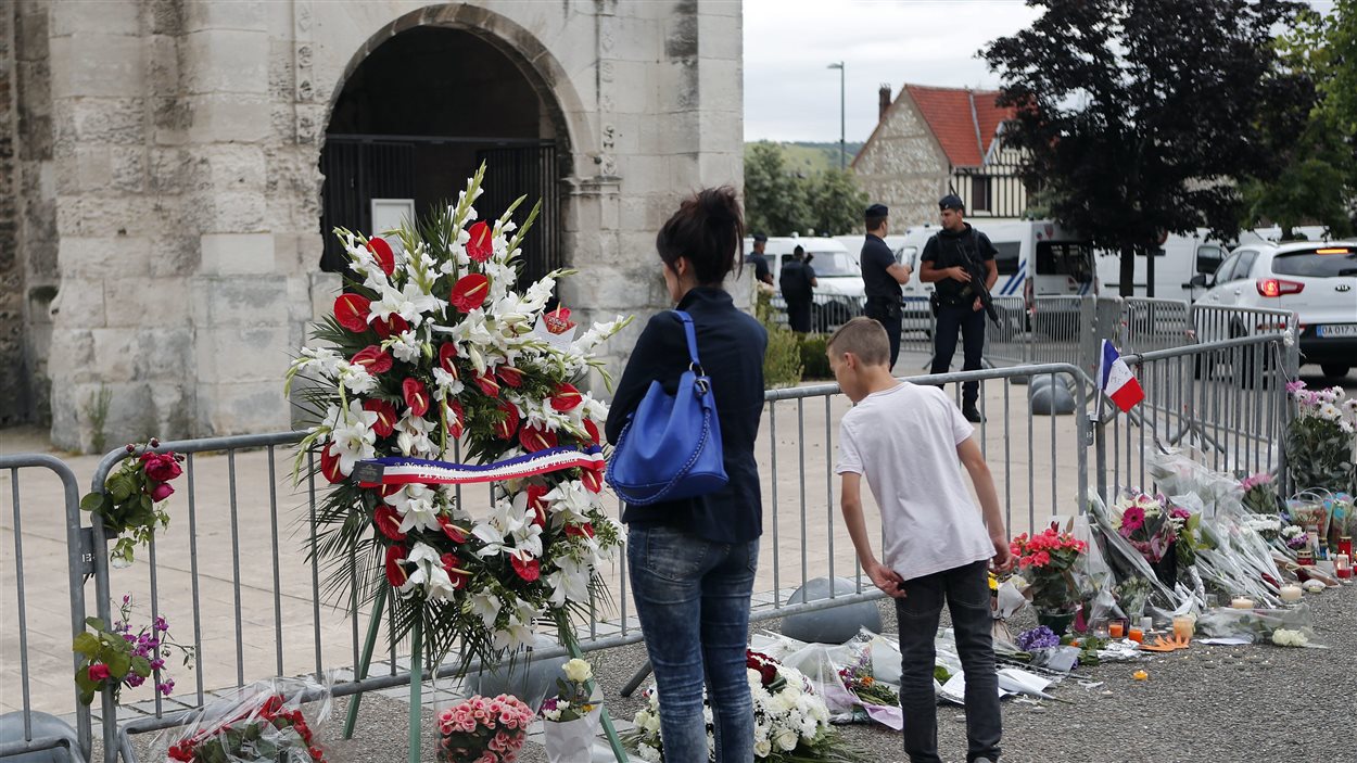 Des gens se recueillent avec des fleurs et des bougies devant l’église normande de Saint-Etienne-du-Rouvray, en Normandie, au lendemain d’une attaque ayant causé la mort d’un prêtre.