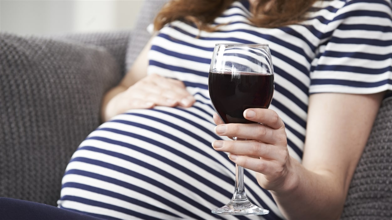 Une femme enceinte tient un verre de vin.
