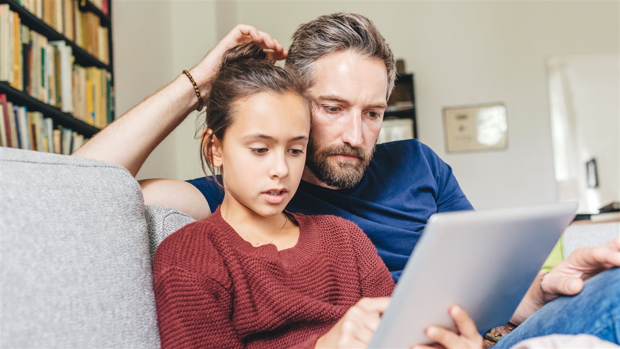Une fille et son père regardent une tablette.