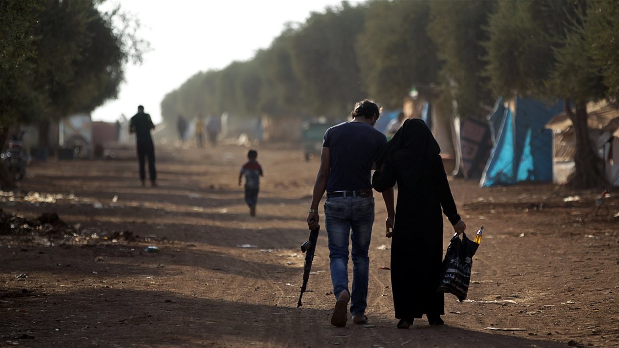 Un homme armé se déplace aux côté d'une femme dans un camp de réfugiés dans le nord d'Alep.