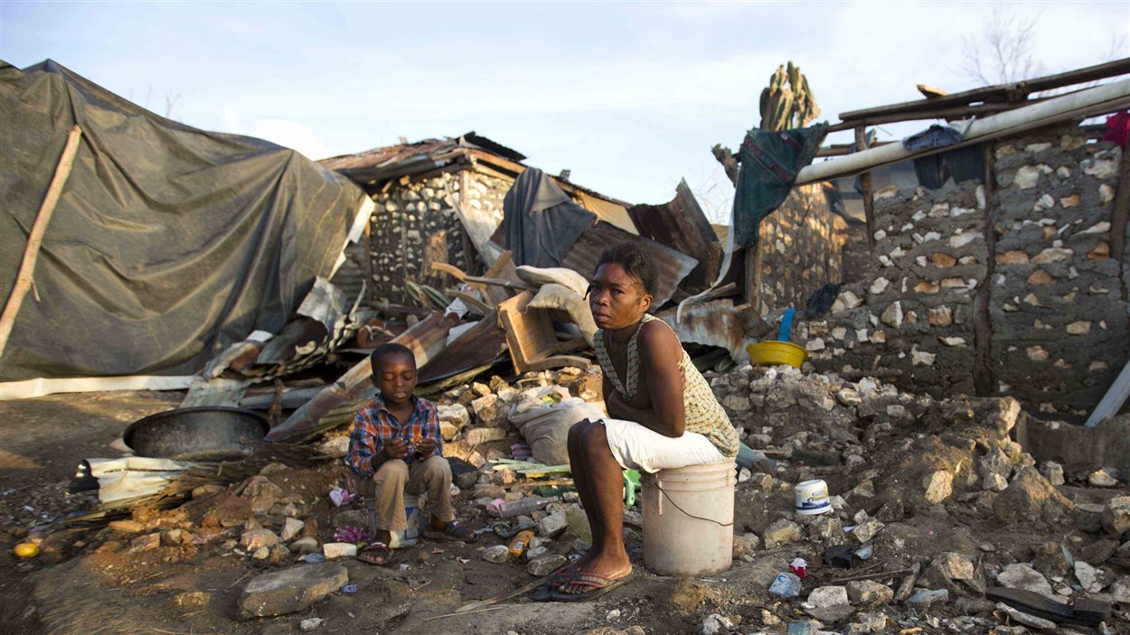 Au milieu des ruines de Jérémie, en Haïti, une femme et un enfant sont assis sur des seaux, dans ce qui était autrefois leur maison.