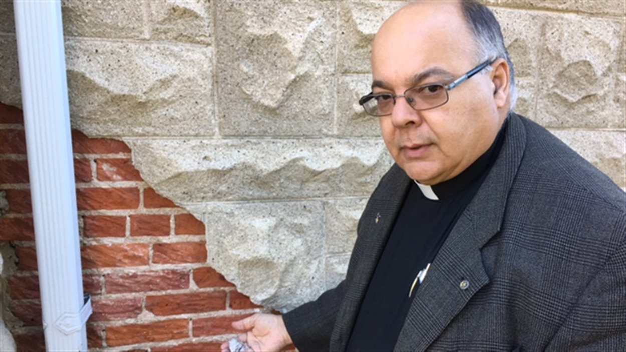 Le père Eugéne Roy montre les murs abîmés de l'église