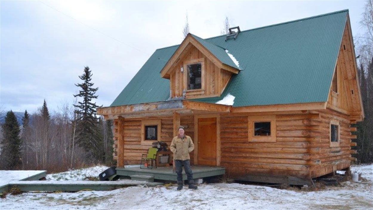 Norm Carlson devant sa maison en rondins