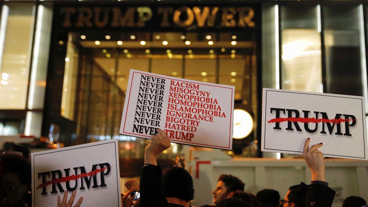 Des gens tiennent des pancartes à bout de bras devant la Trump Tower, dans Manhattan, à New York.