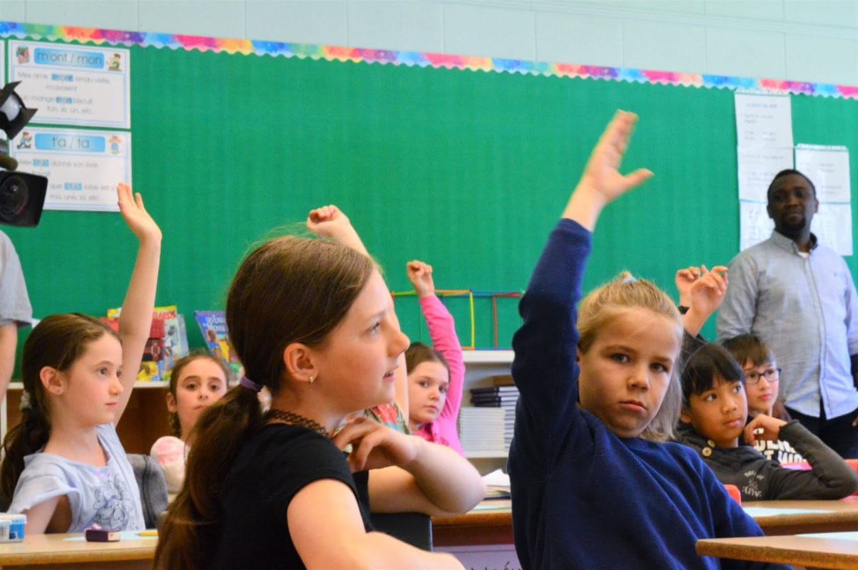 des enfants lèvent leur mains pour participer