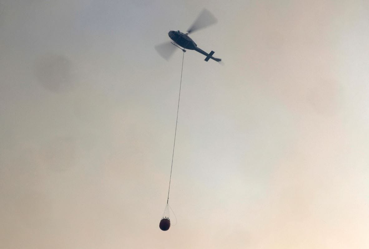 Un hélicoptère transporte un seau d'eau afin d'éteindre les flammes.