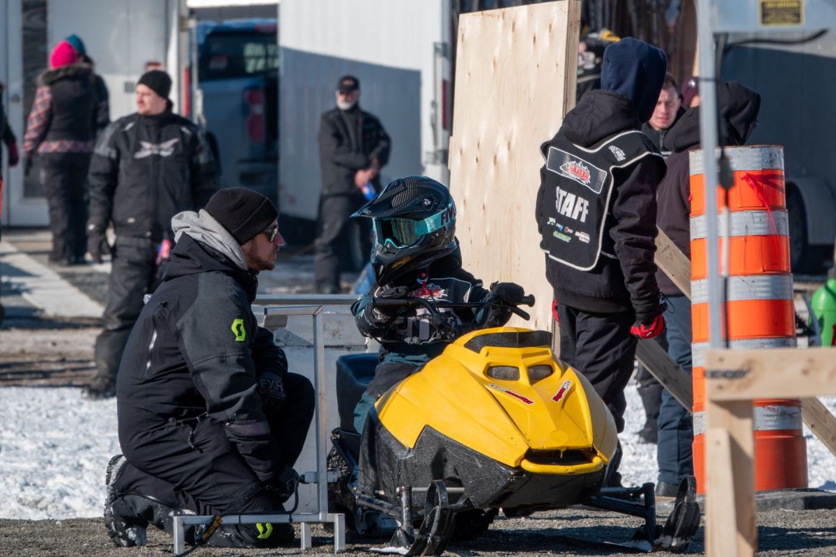 Un enfant se trouve sur une motoneige. Un adulte est accroupi près de lui.