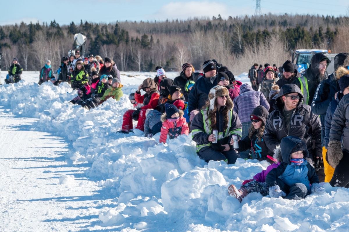 Des gens assis dans la neige en bordure de piste.