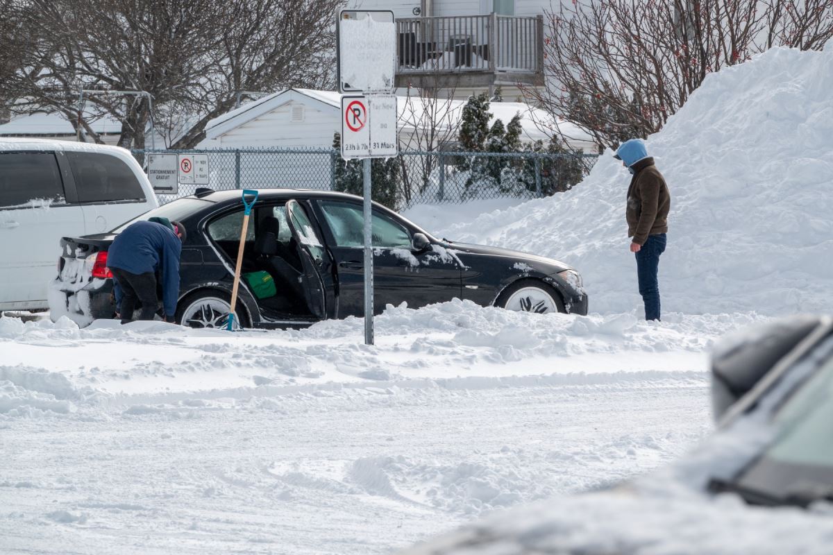 Deux personnes tentent de décoincer une voiture prise dans la neige.