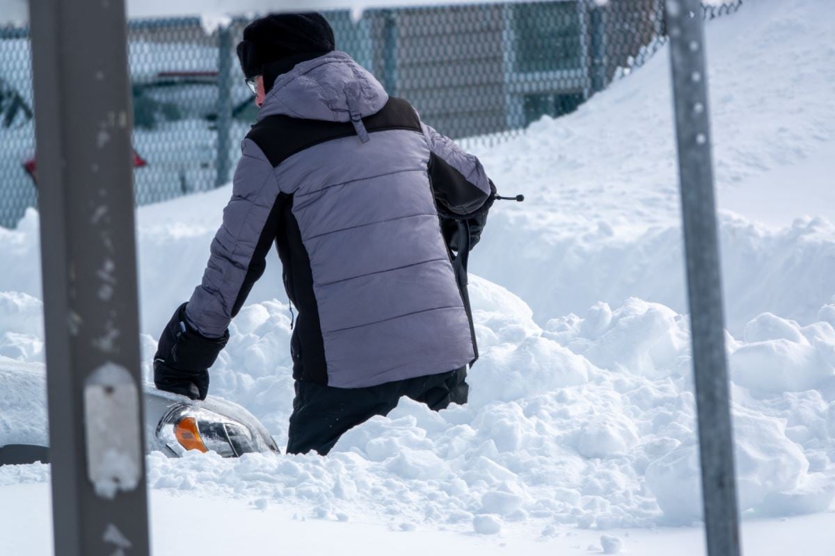 Une personne pelte sa voiture. Elle a de la neige jusqu'aux hanches.