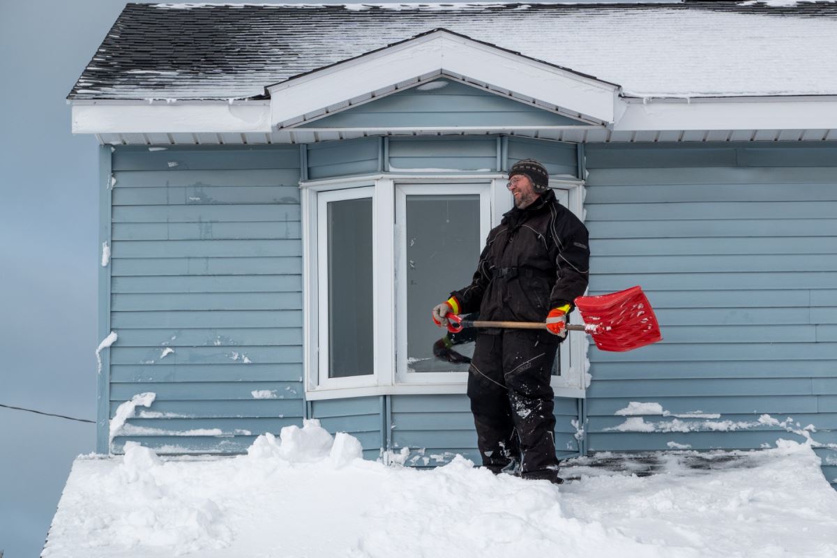 Un homme, debout sur un toit enneigé, sourit en tenant une pelle.