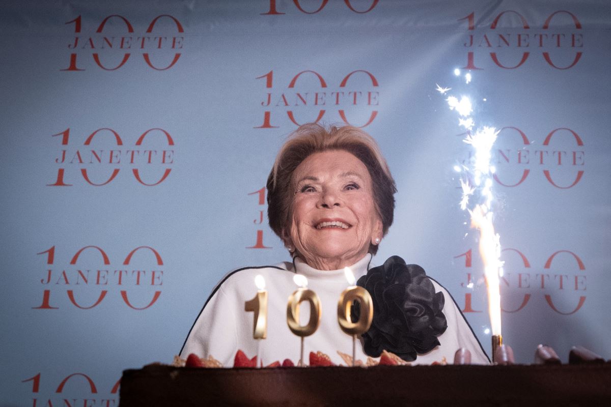Janette Bertrand sourit devant un gâteau sur lequel on voit trois bougies formant le chiffre 100. 